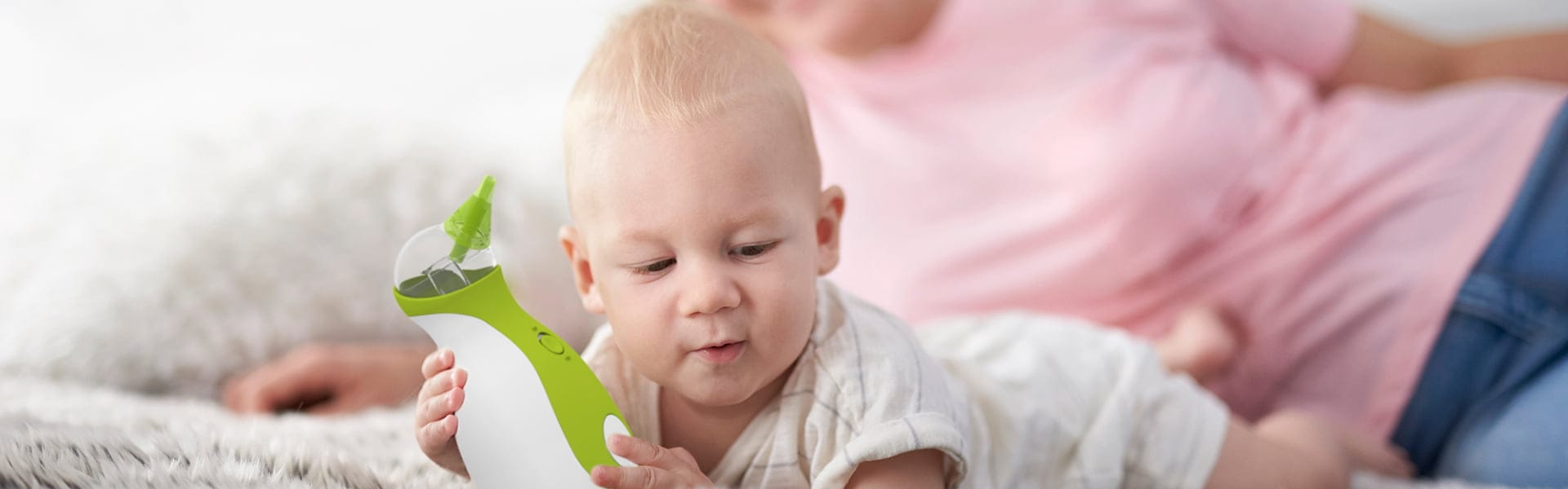 Une mère et un bébé allongés sur un tapis et tenant le mouche-bébé portatif Nosiboo Go