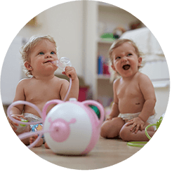 Deux petites filles heureuses assises sur le sol avec un mouche-bébé électrique Nosiboo Pro rose