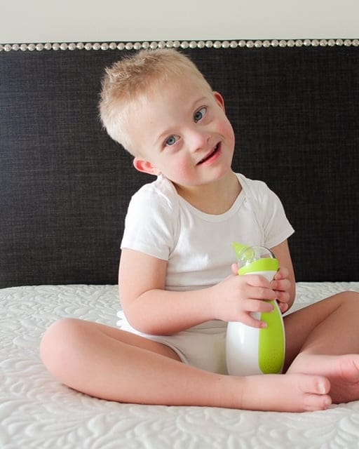 Un petit garçon assis sur le lit, tenant dans ses mains le mouche-bébé portatif Nosiboo Go