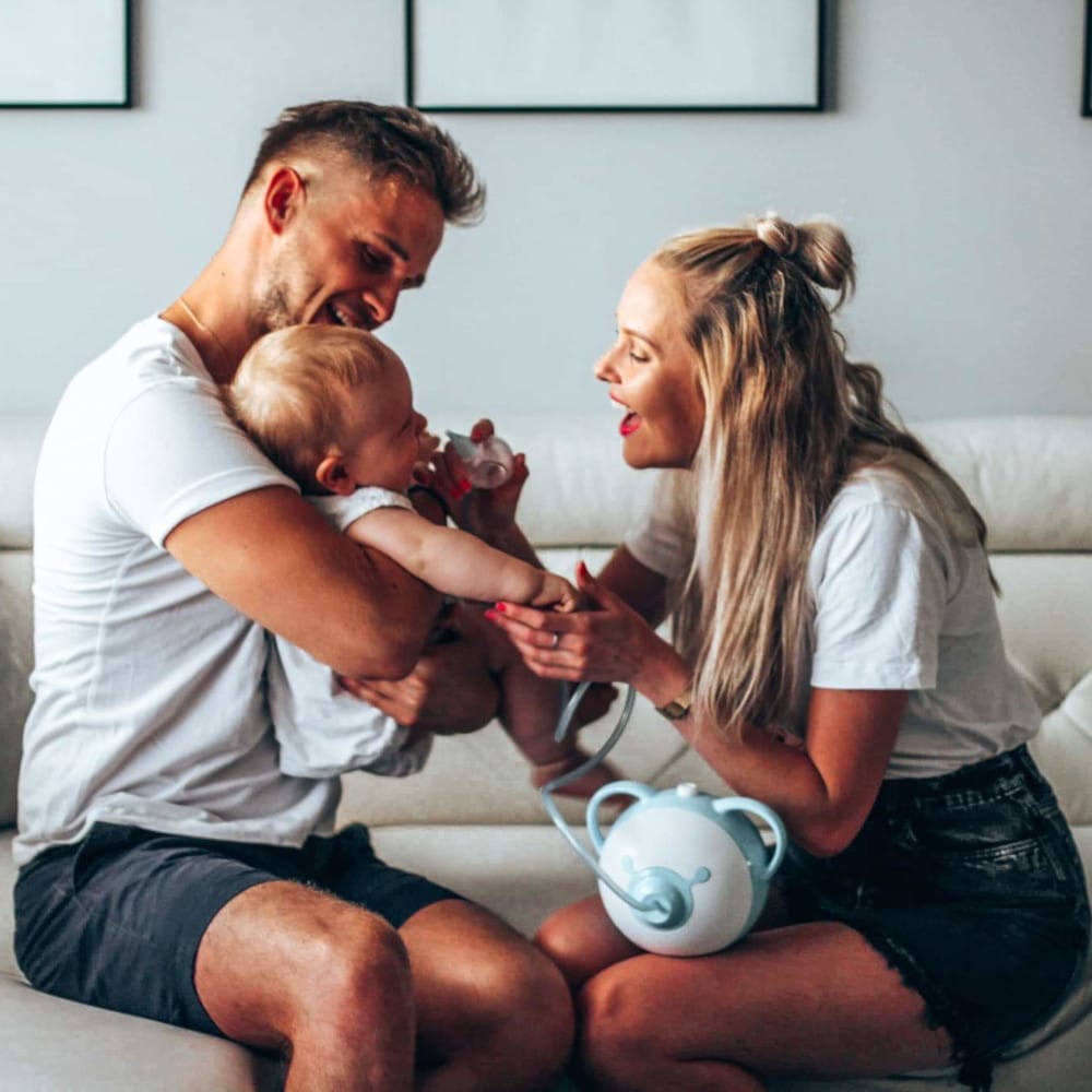 Une mère et un père aspirent ensemble le nez de leur bébé avec le mouche-bébé électrique Nosiboo Pro