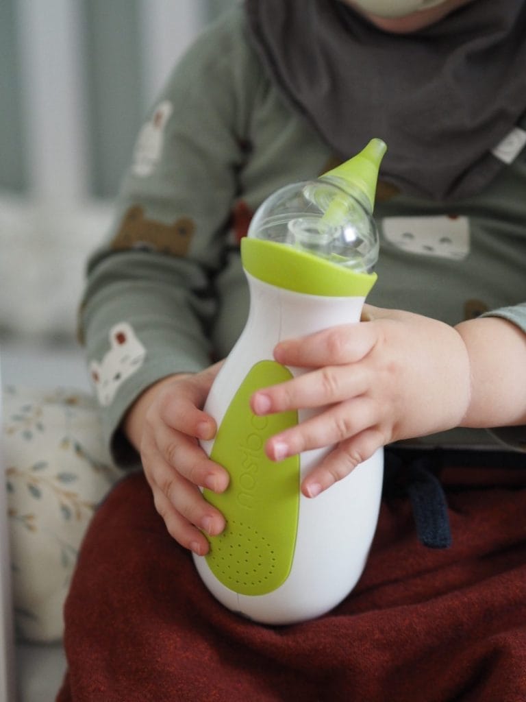 Un petit garçon assis sur le lit, tenant dans ses mains le mouche-bébé portatif Nosiboo Go