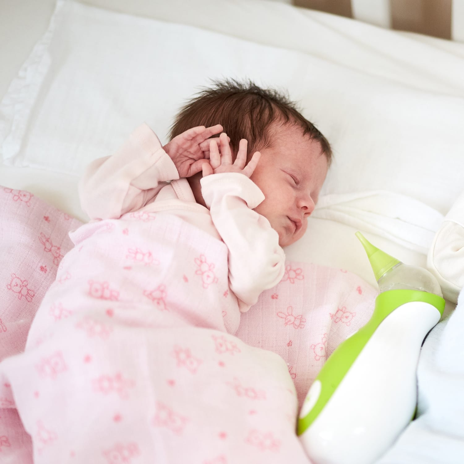 Un nouveau-né dormant dans un lit à côté d'un mouche-bébé portatif Nosiboo Go.