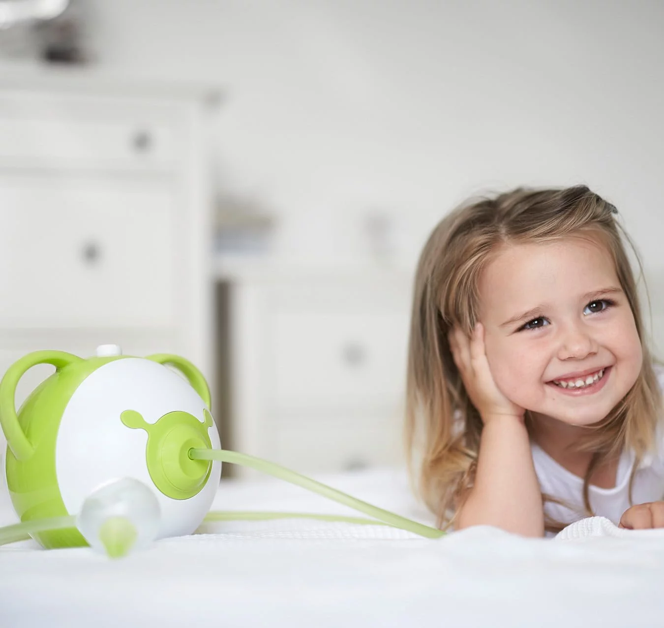 Afficher en taille réelle une photo d'une petite fille souriante allongée sur son lit à côté du mouche-bébé électrique Nosiboo Pro