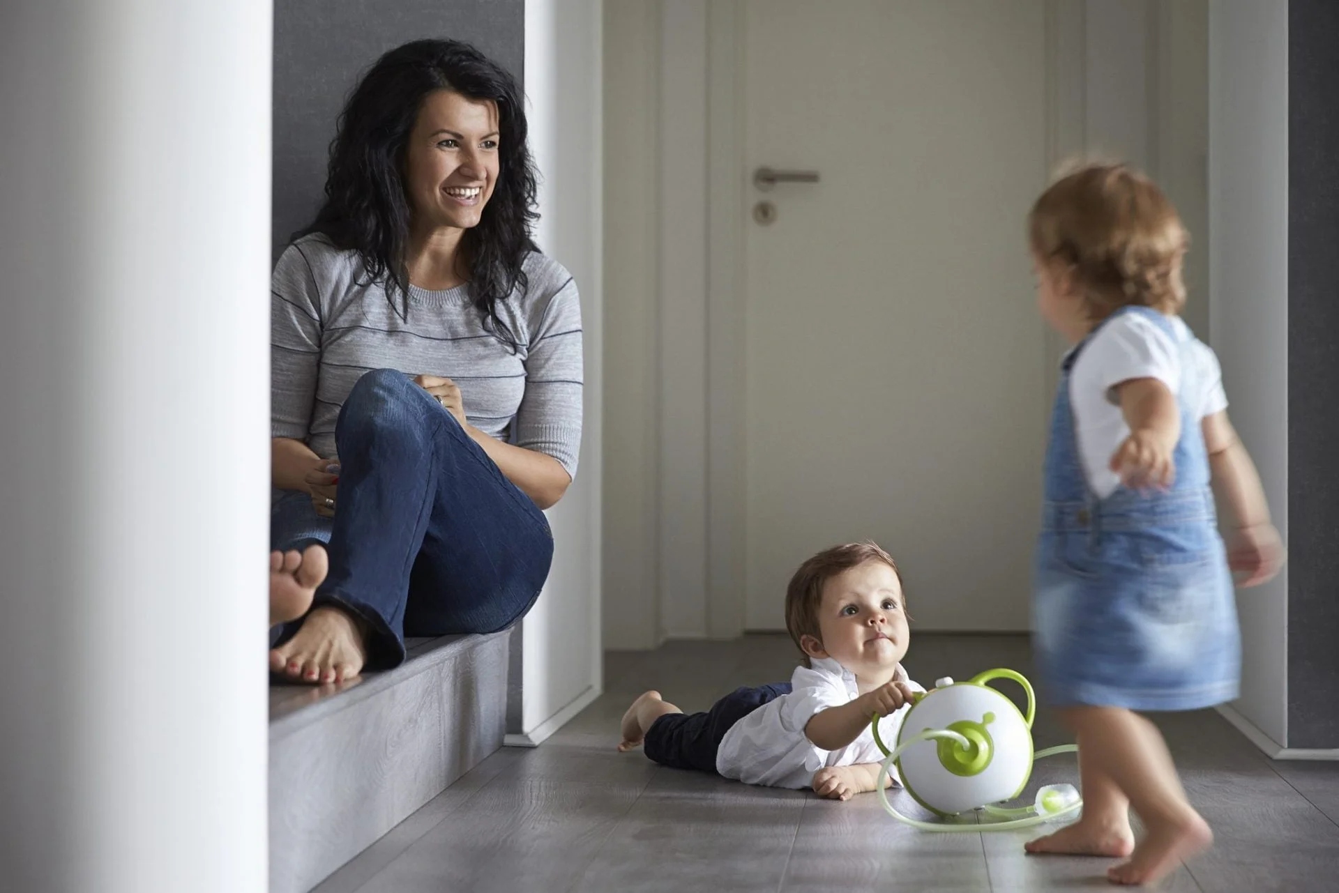 Afficher une photo en taille réelle d'une mère avec deux petits enfants et le mouche-bébé électrique Nosiboo Pro vert dans le couloir de leur maison