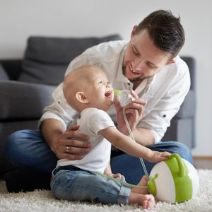 Afficher une photo en taille réelle d'un papa qui nettoie le nez de son bébé souriant à l'aide d'un mouche-bébé électrique Nosiboo Pro vert