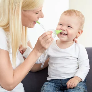 Une mère nettoie le nez de son bébé souriant à l'aide du mouche-bébé manuel Nosiboo Eco