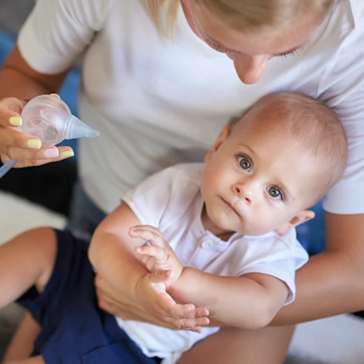 Un petit garçon regarde dans la caméra, tenu par sa mère qui va lui dégager le nez à l'aide du mouche-bébé électrique Nosiboo Pro