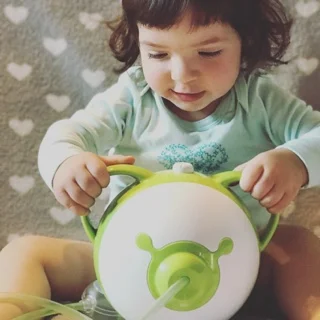 Une petite fille souriante tenant par les oreilles la tête de nounours du mouche-bébé électrique Nosiboo Pro vert