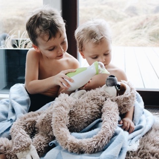 Deux petits garçons jouent avec un animal en peluche en lui nettoyent le nez avec le mouche-bébé portatif Nosiboo Go