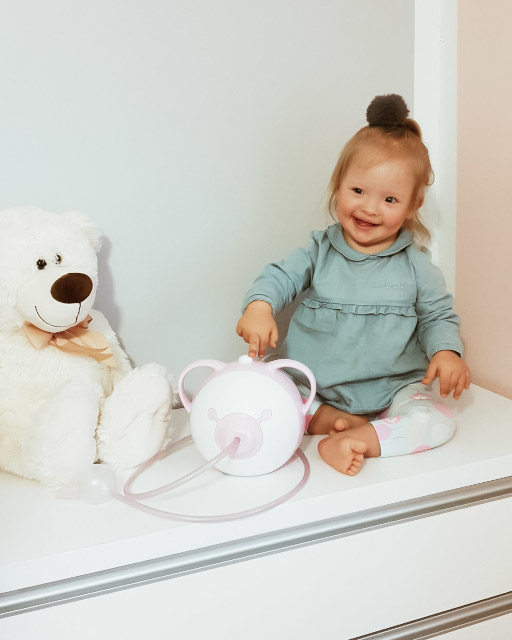 Une petite fille souriante avec un ours en peluche et un mouche-bébé électrique Nosiboo Pro rose