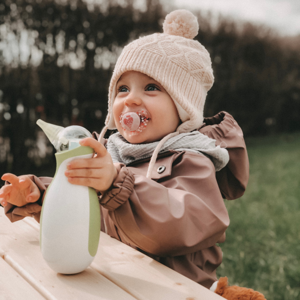 Petite fille en plein air, habillée chaudement, tenant un mouche-bébé électrique portatif Nosiboo Go.