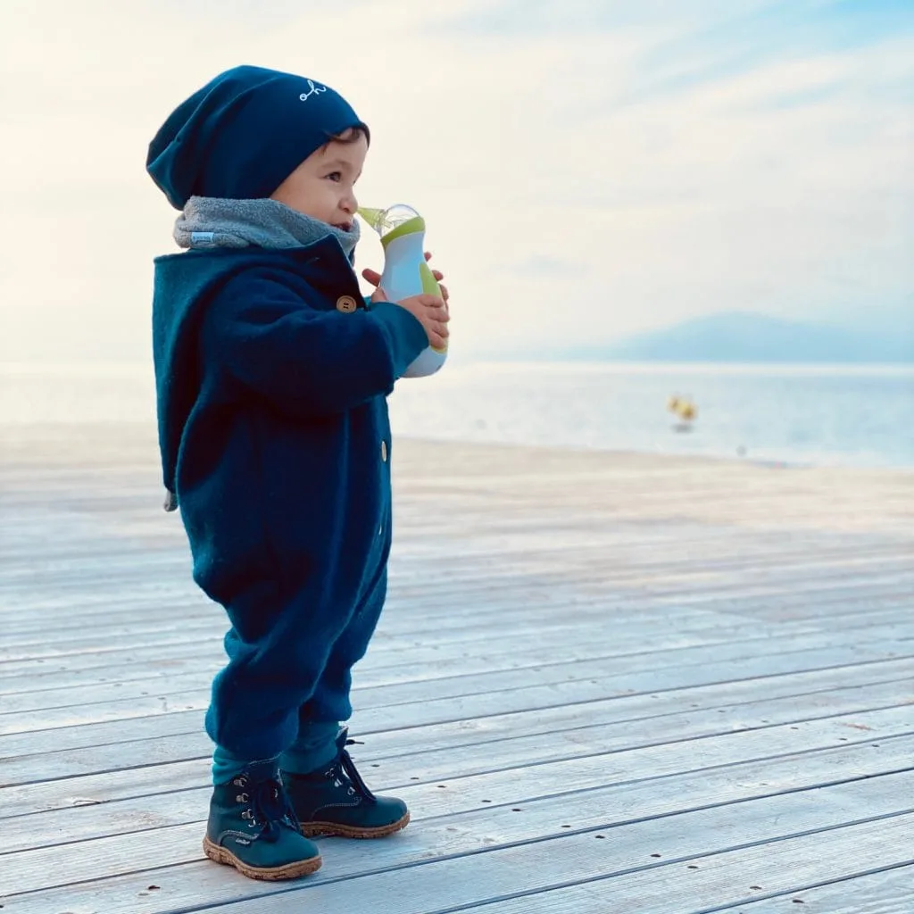 Un petit garçon au bord de l'eau en hiver, tenant un mouche-bébé électrique portatif Nosiboo Go