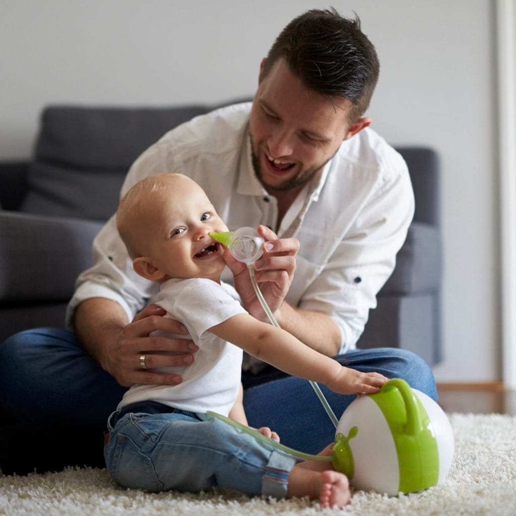 Un père nettoie le nez de son bébé souriant à l'aide du mouche-bébé électrique Nosiboo Pro