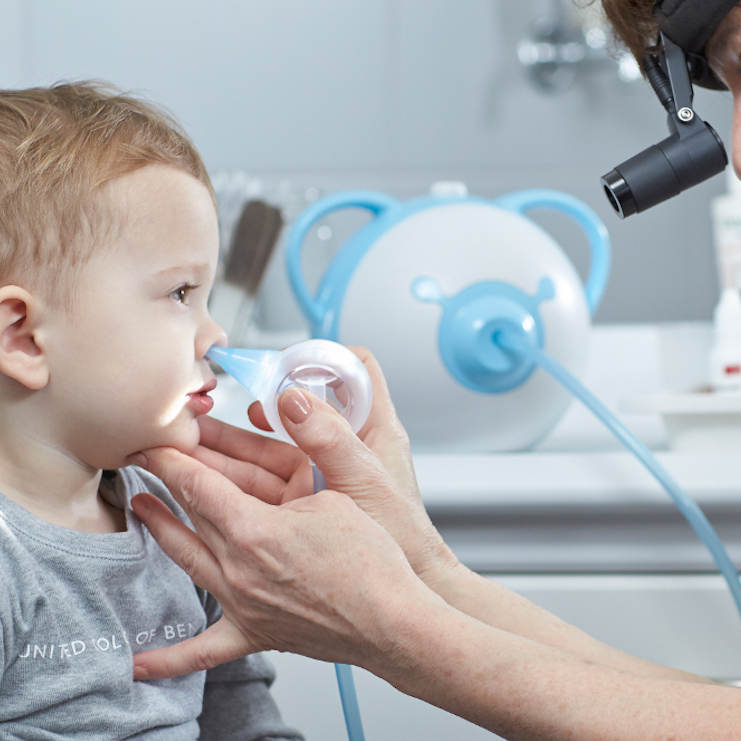 Un ORL nettoie le nez d'un petit garçon à l'aide d'un mouche-bébé électrique Nosiboo Pro.