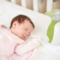 Afficher une photo en taille réelle d'un nouveau-né dormant dans un lit de bébé, à côté d'un mouche-bébé portatif Nosiboo Go