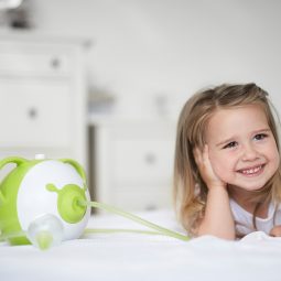 Afficher en taille réelle une photo d'une petite fille souriante allongée sur son lit à côté du mouche-bébé électrique Nosiboo Pro